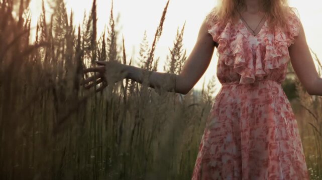 Woman Walking Through Tall Grass Field At Sunset. Summer Evening Atmosphere. Outdoor Relaxation