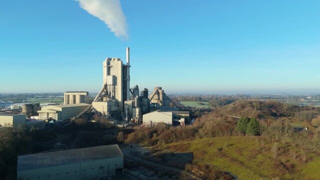 High angle drone shot of smoke billowing from the tall chimney at Rugby Cement Plant.