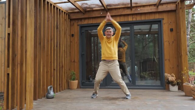 Man doing jumping jacks exercise on wooden terrace at home, active training session improving cardio fitness outdoors