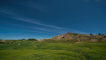 Fototapeta premium Narrow winding white path through open green hillside with rocky cliff and clear deep blue sky scenic nature landscape photography editorial