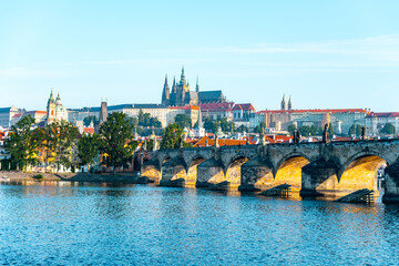 Stunning panorama of Prague with the historic Charles Bridge arching over the Vltava River, framed by the majestic Prague Castle under a clear blue sky, showcasing the city's rich architecture. © pyty