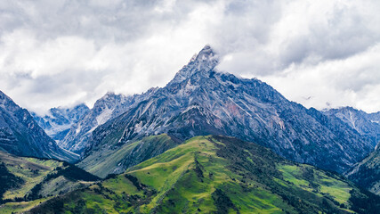 Fototapeta premium Landscape of Mount Genie and alpine grasslands in western Sichuan, China, with dramatic clouds, snow-capped peaks and changing light across the Tibetan Plateau.