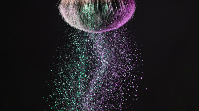 Makeup brush flicking iridescent green and purple cosmetic powder on black background