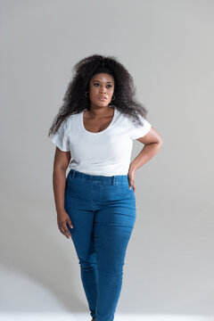 African American woman modeling in studio wearing white ribbed tee blue high-waisted jeans hoops