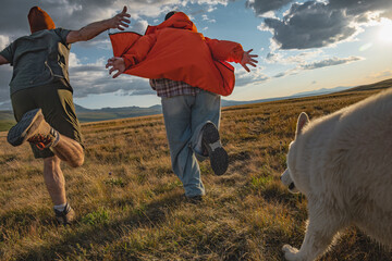 Happy friends running and having fun in a wild field with a big white dog at sunset. Back view of young people enjoying freedom and adventure during a summer trip in the mountains. © ANDREY