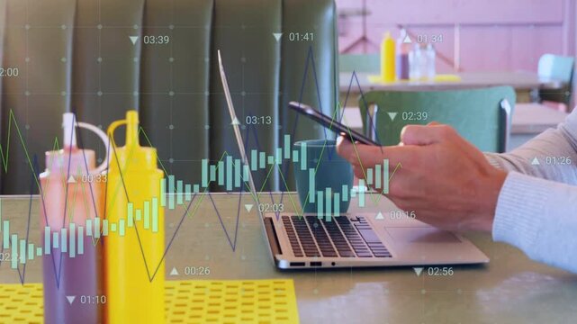 Man pausing typing then reaching phone and checking finance overlay while holding mug in diner