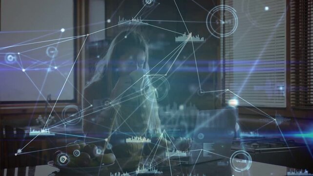 Woman at kitchen counter typing, causing animated HUD graphs overlaying laptop for tech work