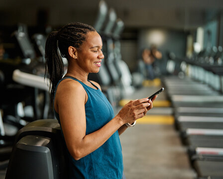 Portrait of a young black woman using a phone ant exting taking a break exercising in a gym, running using  thereadmill machine equipment, healthy lifestyle and cardio exercise at fitness club concept