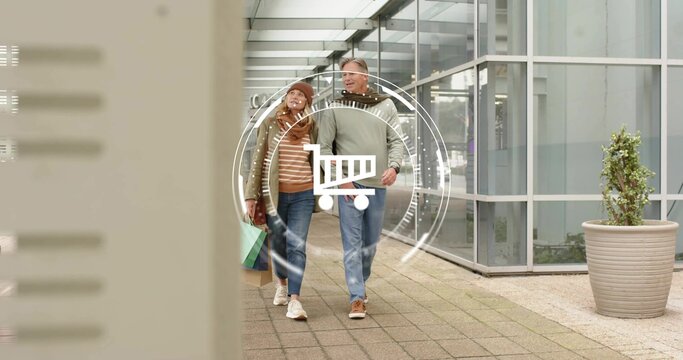 Walking mature couple carrying shopping bags through glass walkway, wearing jackets, cart graphic