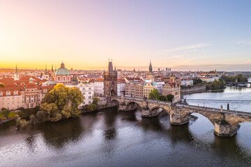 Naklejka premium The Old Town Bridge Tower stands tall against a colorful sunset in Prague. The historic Charles Bridge stretches across the Vltava River, framed by city buildings.