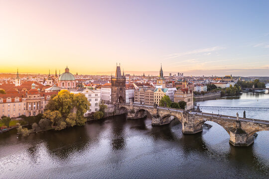 The Old Town Bridge Tower stands tall against a colorful sunset in Prague. The historic Charles Bridge stretches across the Vltava River, framed by city buildings.