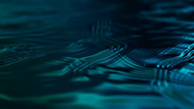 Slow motion tracking close up of water ripples and reflective patterns moving across dark teal surface in studio setting