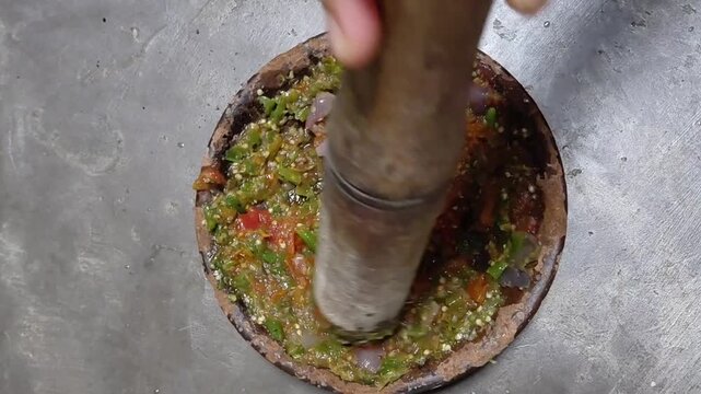Top View of Grinding Fresh Green Chili Sambal in Stone Mortar