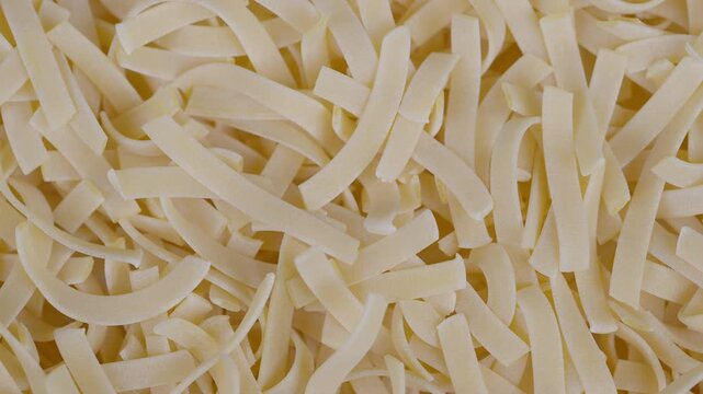 Egg pasta strands with rustic kitchen ambiance. Detailed image capturing pale golden pasta ribbons scattered over rustic kitchen backdrop with natural highlights