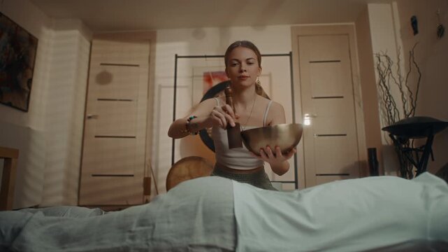 Sound healer playing bowl over client during relaxation therapy