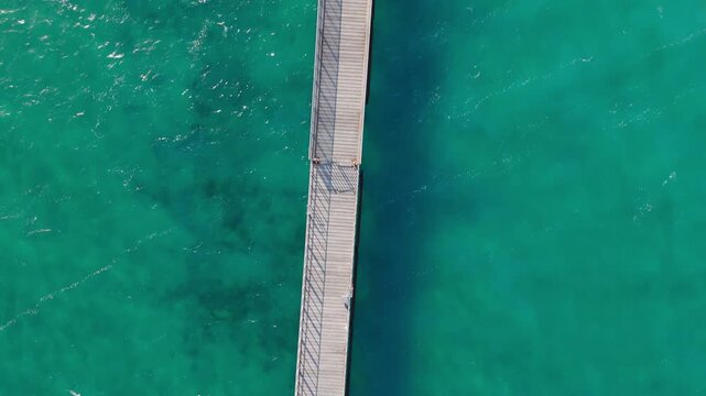 Top Down Drone Perspective of Rustic Wooden Pier and Vibrant Turquoise Sea at Mavralis Beach