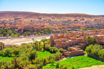 Obraz premium Ait Benhaddou stands along the caravan route. This site shows earthen architecture and traditional village life. Surrounding palm trees and green fields highlight its desert setting.