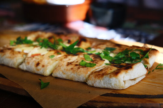 Suluguni cheese in Georgian lavash are served on wooden board, wrapped baked lavash with chopped cilantro, adding a bright, herbaceous note 