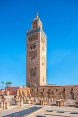 Fototapeta premium Koutoubia Mosque is located in Marrakesh, Morocco. The tall tower reaches up to the blue sky. Visitors admire the mosque's architecture during a sunny day in the city.