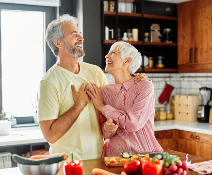 Portrait of happy senior mid aged mature couple prepering meal with fresh vegatebles in kitchen at hpme