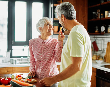 Portrait of happy senior mid aged mature couple prepering meal with fresh vegatebles in kitchen at hpme