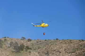 Firefighting rescue helicopter carrying water bucket for wildfire over mountains in Benidorm, Spain © Montana82