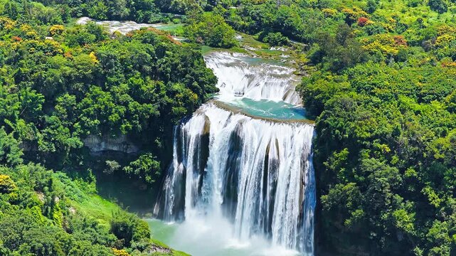Aerial view of Huangguoshu waterfall cascading down rocky cliffs surrounded by lush green forest in Anshun, Guizhou, China