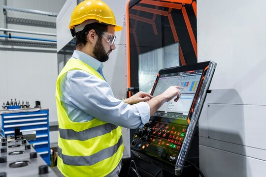 Focused engineer wearing hardhat using touch screen machine at factory
