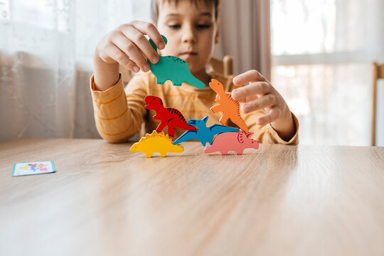 Boy stacking a colorful wooden dinosaur toy on a table indoors