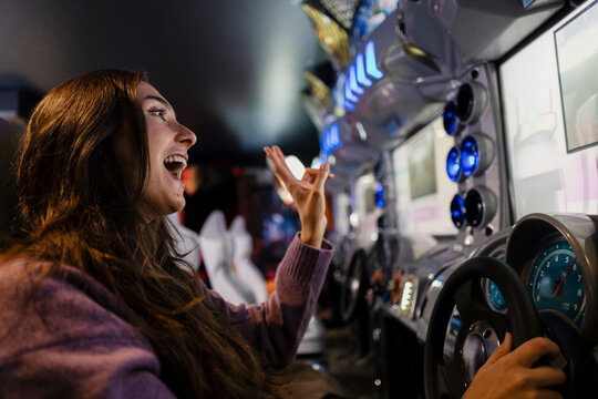 Excited woman playing racing video game at indoor arcade