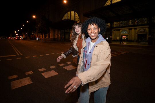 Smiling friends having fun walking on a city street at night