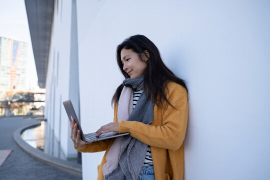 Freelancer in yellow cardigan typing on laptop outdoors