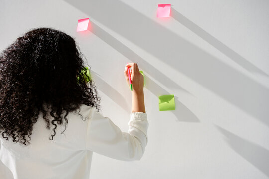 Rear view of employee writing on sticky notes during brainstorming