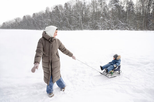 Parent pulling child on sled in snowy winter landscape