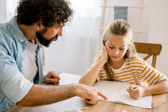Father helping child with homework at home sitting at table