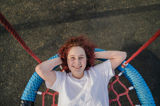 Person relaxing on a web swing at an outdoor playground smiling