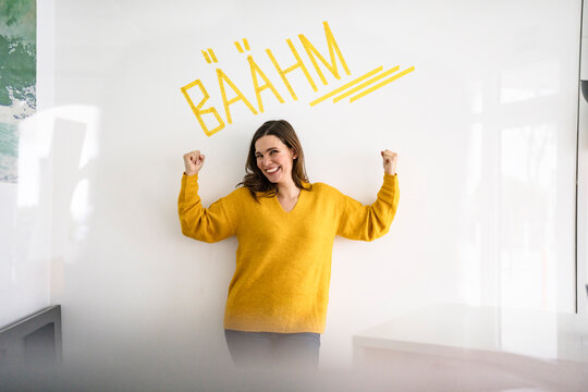 Creative businesswoman flexing muscles in front of wall with text in office