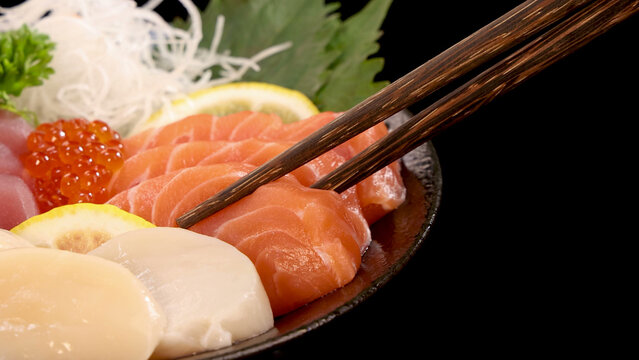 Wooden Chopsticks Picking Up Fresh Salmon Sashimi From a Sushi Platter