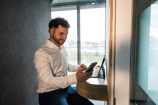 Businessman using mobile phone in modern office privacy booth