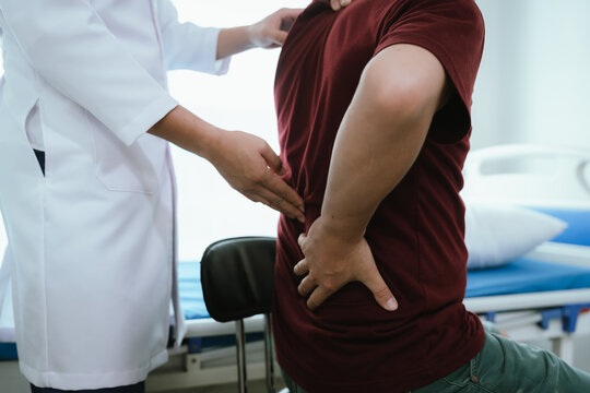 Doctor explaining spine anatomy with a model to a male patient experiencing lower back pain in a clinic, discussing diagnosis and treatment options.