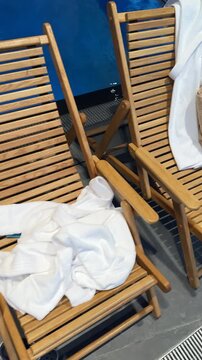 Fluffy bath towels neatly folded atop wooden sun loungers beside the pool, ready for spa guests in a serene wellness retreat.