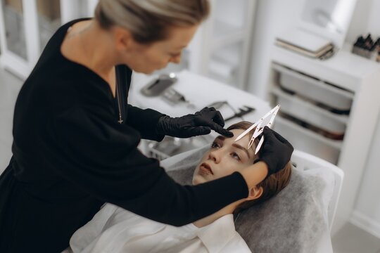 Beautician measuring client's eyebrows for microblading treatment