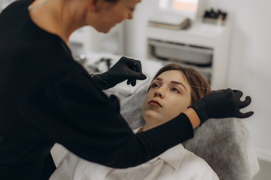 Cosmetologist threading eyebrows on young woman in beauty salon