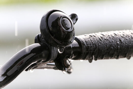 降りしきる雨に濡れた自転車のハンドルとベルに付いた水滴
