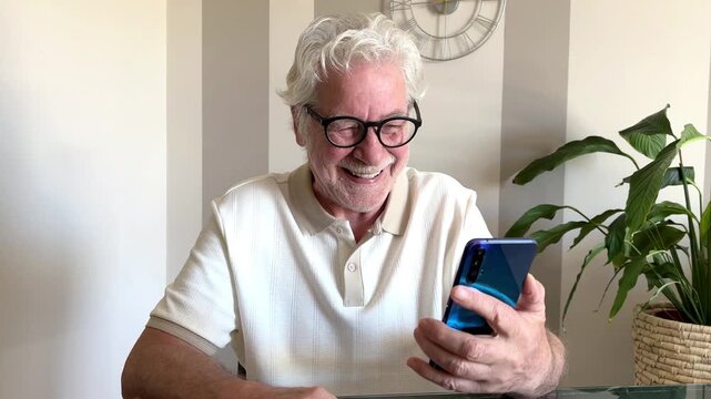 An elderly man finds joy and connection while laughing heartily at his smartphone. He enjoys digital communication and stays connected with family or friends. This scene portrays modern senior living.