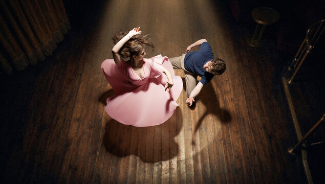 Top view of couple dancing lindy hop on wooden floor under warm spotlight with flowing dress and strong shadows. Concept of vintage lifestyle, dance performance for entertainment and events.