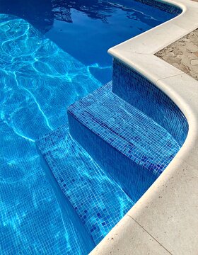 Close-up of a vibrant blue tiled pool with integrated steps, a white coping edge, and shimmering water