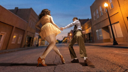 Obraz premium Couple dancing lindy hop on empty street at dusk under warm street lights with low angle view and motion. Concept of romance, vintage lifestyle, travel and nightlife entertainment.
