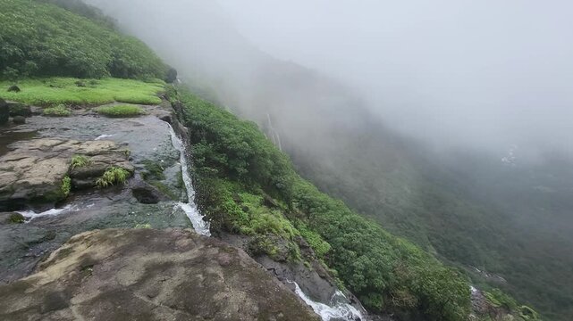 A roaring Sahyadri waterfall descends near majestic Kulang Fort, wrapped in clouds, rugged cliffs, and vibrant green valleys. A stunning 4K capture of monsoon magic and wild mountain beauty.