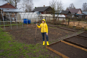 Fototapeta premium a girl in a yellow jacket and rubber boots in the garden with a shovel in her hands